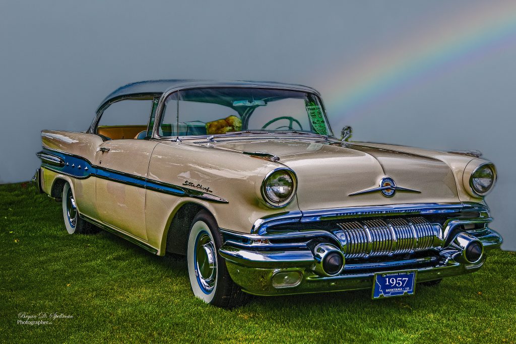 The iconic 1957 Pontiac Star Chief, photographed here parked on a green grass lawn against a dark sky with a rainbow.
