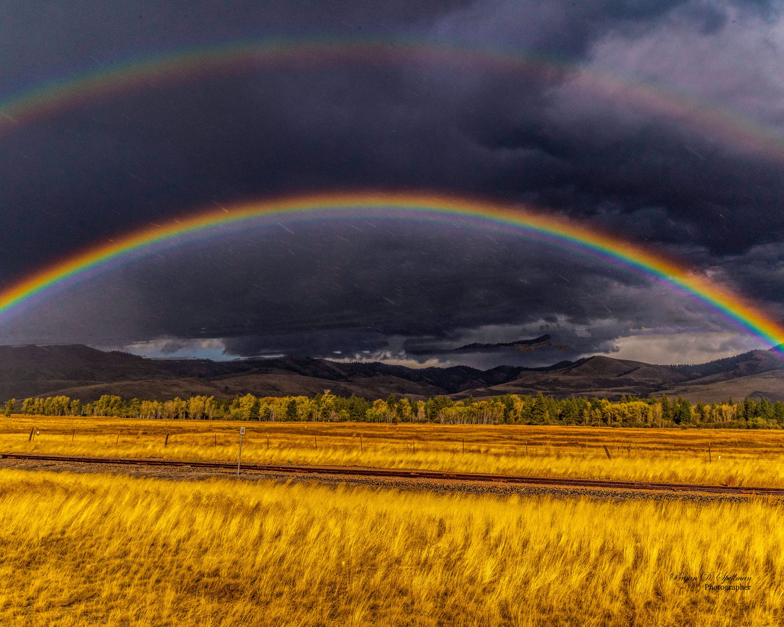 A double rainbow in a dark sky over a golden hayfield